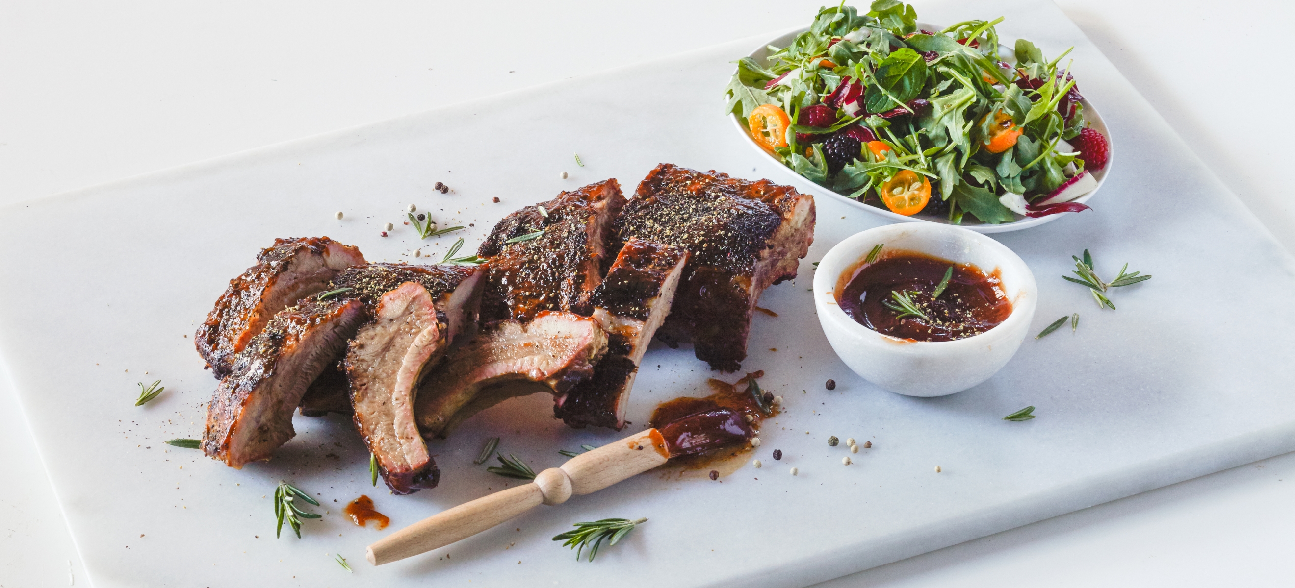 a rectangular white platter holding baby back ribs, rib sauce, and a salad