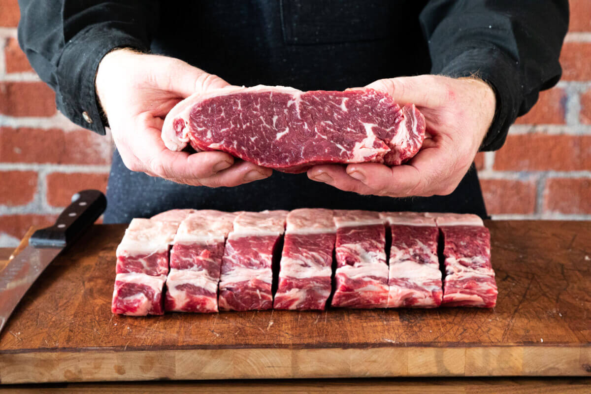 man holding steak over steaks on a cutting board