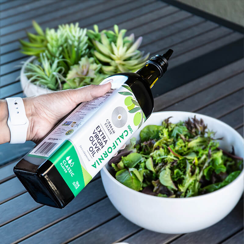 Bottle of extra virgin olive oil being poured over salad