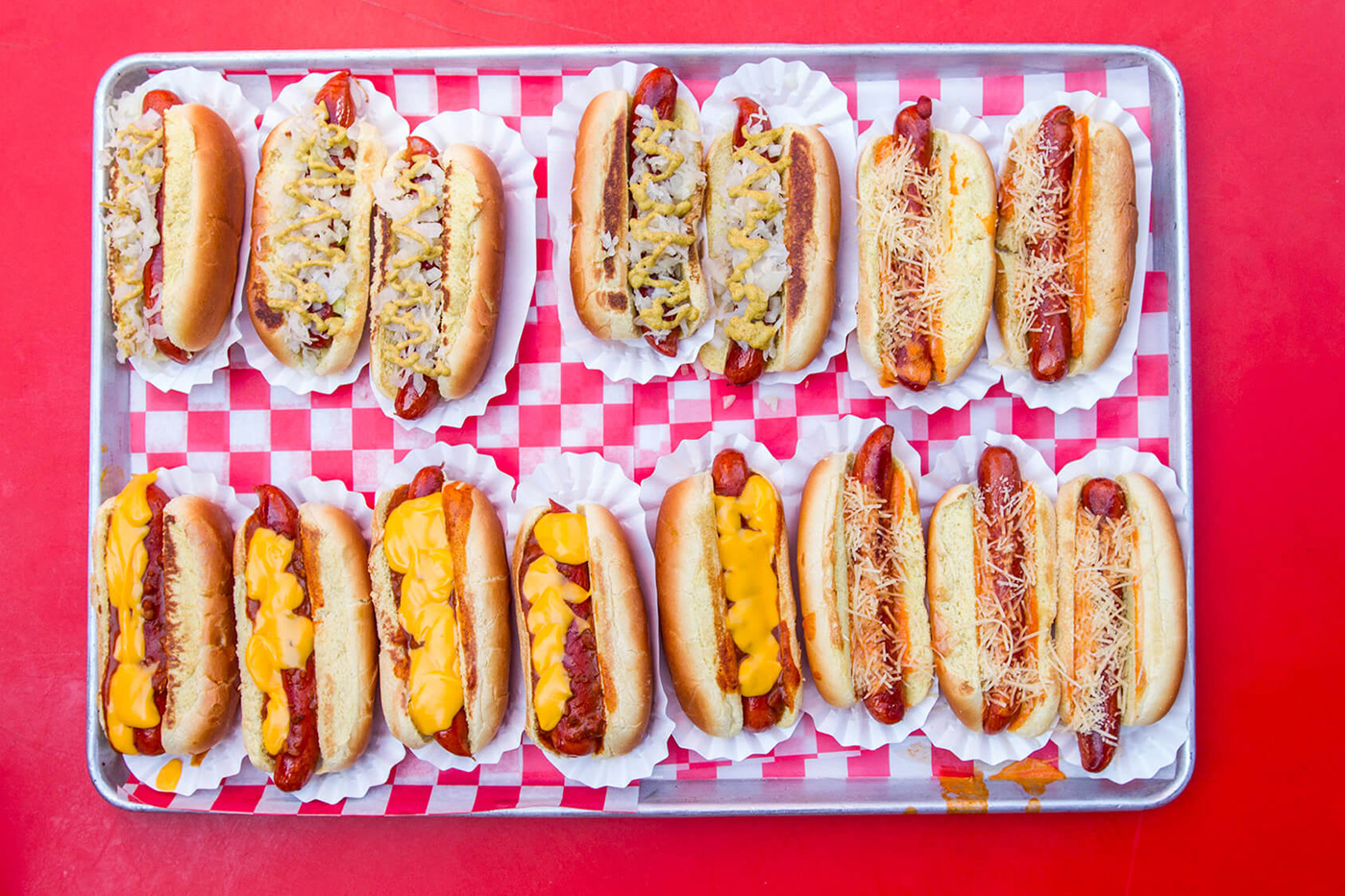 2 rows of garnished hot dogs on a checkerboard lined sheet pan