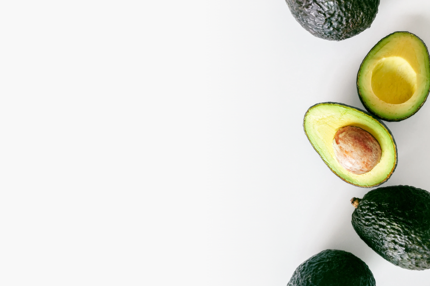 3 whole avocados and one avocado cut in half on a white background